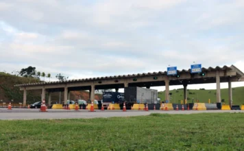 Pedágios de SC podem ter pista exclusiva para motos Vista frontal de uma praça de pedágio em rodovia de Santa Catarina com cabines de atendimento, sinalização de cobrança automática e cones de segurança. A imagem ilustra o cenário das concessões catarinenses que deverão implementar pistas exclusivas para motocicletas conforme o projeto de lei aprovado pela Comissão de Trabalho da Alesc.