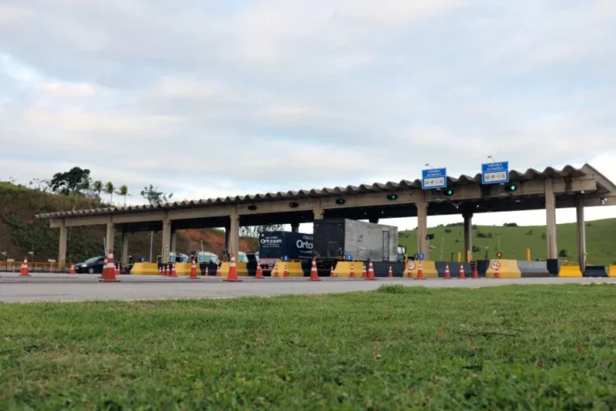 Pedágios de SC podem ter pista exclusiva para motos Vista frontal de uma praça de pedágio em rodovia de Santa Catarina com cabines de atendimento, sinalização de cobrança automática e cones de segurança. A imagem ilustra o cenário das concessões catarinenses que deverão implementar pistas exclusivas para motocicletas conforme o projeto de lei aprovado pela Comissão de Trabalho da Alesc.