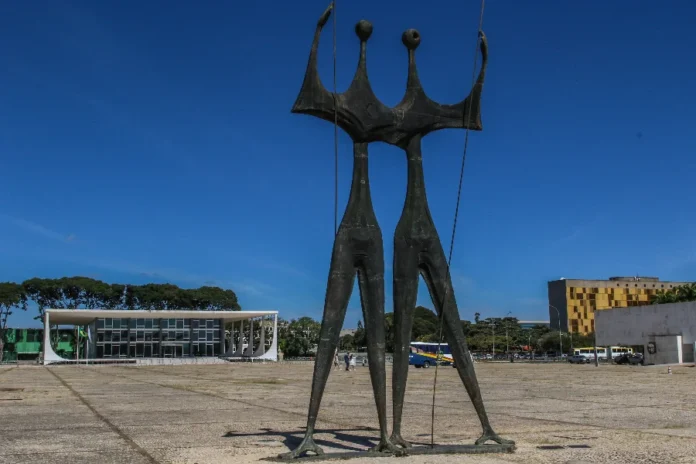 Pensões no STF custam R$ 4,8 milhões por ano aos cofres Escultura Os Candangos em destaque na Praça dos Três Poderes, com o edifício do Supremo Tribunal Federal (STF) ao fundo em Brasília. A imagem ilustra a sede da Corte que despende R$ 4,8 milhões anuais em pensões para dependentes de ex-ministros e servidores.