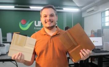 Pesquisa na Unesc transforma restos de madeira em lucro O pesquisador Mateus Alexandre Floriano sorri enquanto segura duas amostras de painéis de madeira de pinus reaproveitadas, em um laboratório da Unesc. A imagem ilustra o estudo de economia circular para o reaproveitamento de resíduos sólidos na indústria de portas do Sul catarinense.