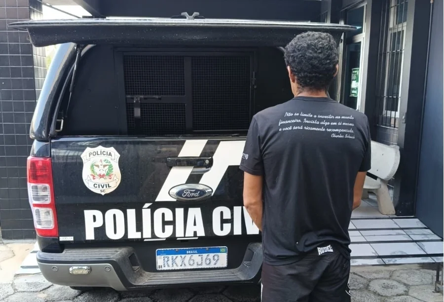 Homem de costas ao lado de viatura da Polícia Civil de Santa Catarina em Turvo, detido por suspeita de matar tamanduá e praticar violência doméstica.
