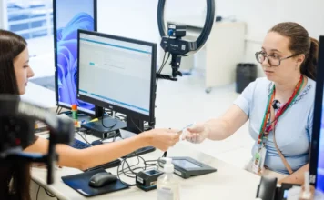 Prazo para regularizar título termina em maio; veja datas Atendimento de jovem eleitora em cartório do TRE-SC para alistamento eleitoral. Funcionária entrega cartão de título de eleitor em mesa com equipamento de biometria. Foto para matéria sobre jovens eleitores em Santa Catarina.