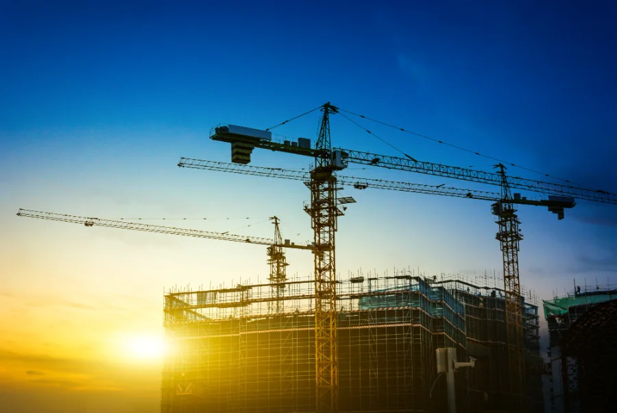Canteiro de obras com silhueta de guindastes e prédios em construção sob o pôr do sol em Santa Catarina. Imagem ilustrativa sobre o aumento de custos na construção civil e os impactos no mercado imobiliário.