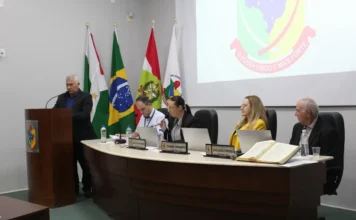 Reginaldo Araújo assume vaga na Câmara de Forquilhinha Reginaldo Araújo Netto discursa na tribuna durante sua posse como vereador na Câmara Municipal de Forquilhinha, em sessão presidida por Laísa Figueredo com bandeiras ao fundo.