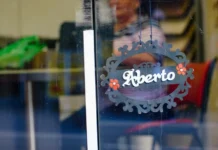 SC abre mais de 45 mil novas empresas no início de 2026 Placa decorativa com a palavra "Aberto" pendurada em uma porta de vidro de estabelecimento comercial, simbolizando a abertura de novas empresas e o fortalecimento do empreendedorismo em Santa Catarina no início de 2026.