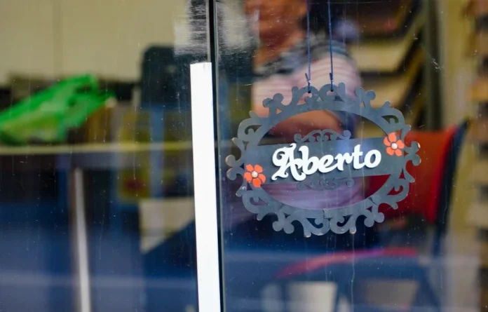 SC abre mais de 45 mil novas empresas no início de 2026 Placa decorativa com a palavra "Aberto" pendurada em uma porta de vidro de estabelecimento comercial, simbolizando a abertura de novas empresas e o fortalecimento do empreendedorismo em Santa Catarina no início de 2026.