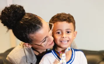 SC amplia leis e auxílio financeiro para mães atípicas Nadynne Chagas abraça o filho Matheus, uma criança com autismo nível 3 que utiliza um cordão de quebra-cabeça, simbolizando a rede de apoio e as políticas para mães atípicas em Santa Catarina.