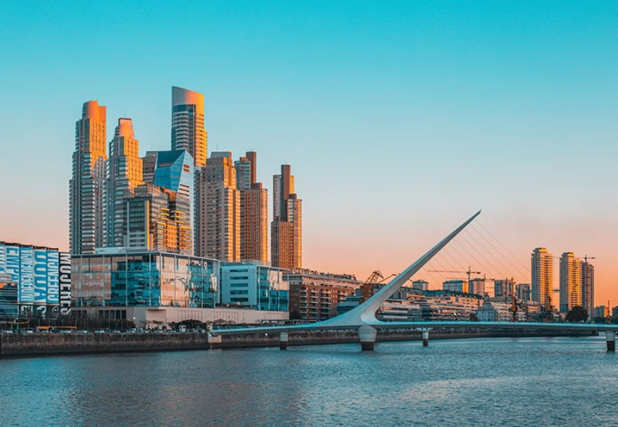 Vista panorâmica de Puerto Madero, Buenos Aires, com a Puente de la Mujer ao pôr do sol. O moderno bairro de negócios da capital argentina brilha com luz dourada, simbolizando o novo clima de negócios e as oportunidades comerciais para exportadores brasileiros, como as indústrias de Santa Catarina, que estão ampliando sua presença no mercado vizinho.