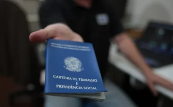 SC cria 16,8 mil empregos em março com força do comércio Pessoa segurando uma Carteira de Trabalho e Previdência Social (CTPS) azul em primeiro plano, simbolizando a abertura de novas vagas e a geração de emprego formal em Santa Catarina.