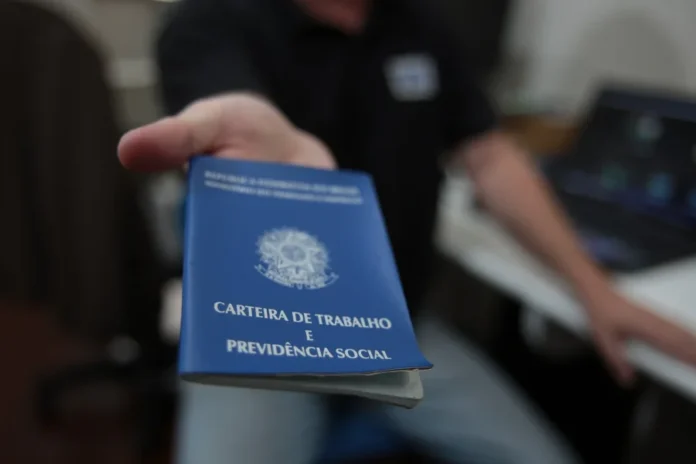 SC cria 16,8 mil empregos em março com força do comércio Pessoa segurando uma Carteira de Trabalho e Previdência Social (CTPS) azul em primeiro plano, simbolizando a abertura de novas vagas e a geração de emprego formal em Santa Catarina.