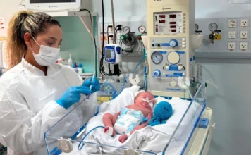 SC distribui 5.173 doses contra vírus respiratório Profissional de saúde com máscara e luvas prepara o anticorpo monoclonal nirsevimabe em seringa ao lado de bebê prematuro em incubadora hospitalar em Santa Catarina. A imagem ilustra a prevenção contra o Vírus Sincicial Respiratório (VSR) em recém-nascidos vulneráveis.