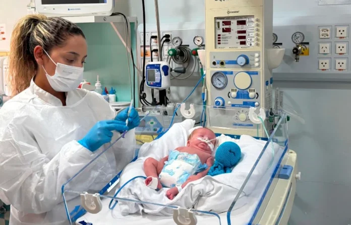 SC distribui 5.173 doses contra vírus respiratório Profissional de saúde com máscara e luvas prepara o anticorpo monoclonal nirsevimabe em seringa ao lado de bebê prematuro em incubadora hospitalar em Santa Catarina. A imagem ilustra a prevenção contra o Vírus Sincicial Respiratório (VSR) em recém-nascidos vulneráveis.