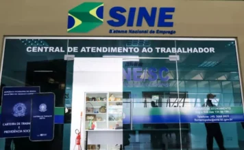 SC inicia semana com 8.645 vagas de emprego pelo Sine Fachada de vidro da entrada de uma unidade do Sine em Santa Catarina, exibindo a logomarca do Sistema Nacional de Emprego e a frase Central de Atendimento ao Trabalhador. Ao lado da porta, há um adesivo ilustrativo da Carteira de Trabalho Digital.