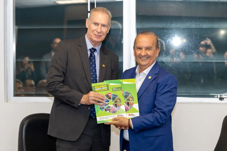 Governador Jorginho Mello entrega o relatório impresso do Balanço Geral 2025 de Santa Catarina ao presidente do TCE/SC, Herneus de Nadal. A imagem ilustra a transparência na gestão das contas públicas estaduais e o cumprimento de metas fiscais.