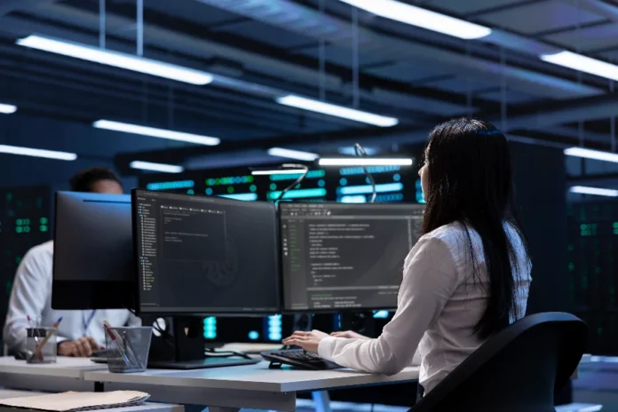 SENAI SC abre ciclo de palestras gratuitas sobre software Desenvolvedora de software trabalhando em frente a monitores com códigos de programação em ambiente tecnológico, representando a capacitação gratuita do programa SCTEC do SENAI/SC para o mercado de TI em Santa Catarina.