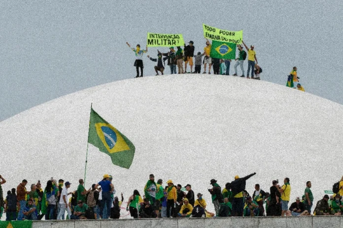 STF anula acordos de 39 réus dos atos de 8 de janeiro Manifestantes ocupam a cúpula do Congresso Nacional em Brasília durante os atos de 8 de janeiro; cena mostra pessoas com camisas do Brasil e faixas pedindo intervenção militar sobre o prédio branco em formato de domo.