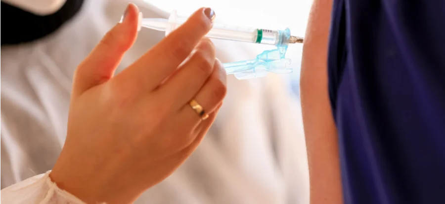 Profissional de saúde aplicando uma vacina no braço de um paciente, imagem ilustrativa sobre a importância da vacinação contra o sarampo para viajantes brasileiros da Copa do Mundo 2026.