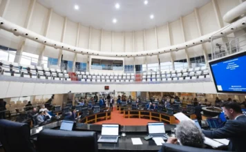 Saúde e infraestrutura marcam debates na Assembleia de SC Vista em grande angular do plenário circular da Assembleia Legislativa de Santa Catarina (Alesc) durante uma sessão parlamentar movimentada, mostrando deputados sentados em suas bancadas, servidores com laptops em primeiro plano e uma grande tela exibindo informações sobre a 38ª Sessão Plenária Ordinária.