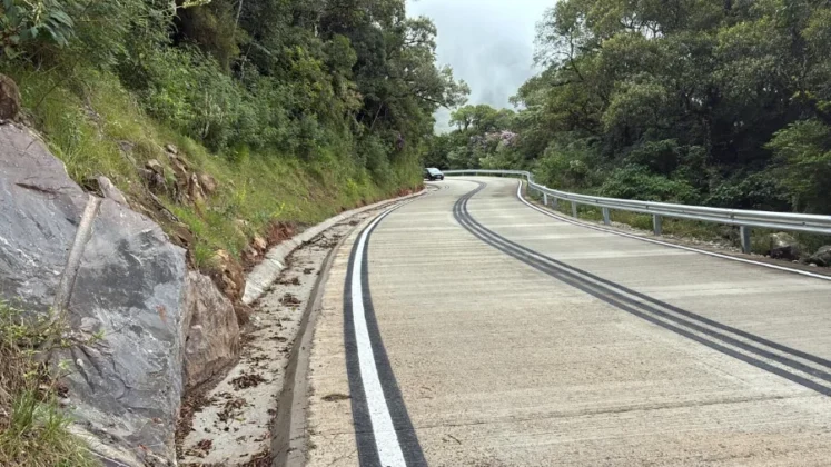 Foto da rodovia SC-290 pavimentada em concreto na Serra do Faxinal, mostrando o grande talude rochoso e a sarjeta de conten&ccedil;&atilde;o ao lado esquerdo e guard-rail &agrave; direita.