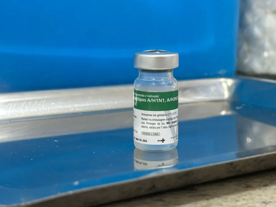 Frasco de vidro da vacina contra a gripe influenza tipos A/H1N1 e A/H3N2 posicionado sobre uma bandeja de inox em Unidade Básica de Saúde de Siderópolis.