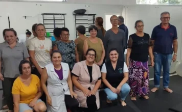 Timbé do Sul realiza ação contra hipertensão arterial Profissionais de saúde da ESF São Luiz e pacientes reunidos na Academia da Saúde em Timbé do Sul durante ação de prevenção e combate à hipertensão arterial. O grupo posa para foto em uma sala com equipamentos de fisioterapia e espelhos ao fundo.
