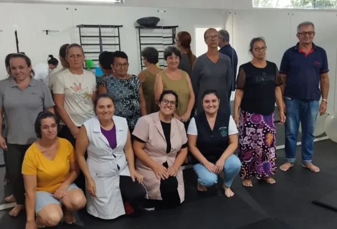 Timbé do Sul realiza ação contra hipertensão arterial Profissionais de saúde da ESF São Luiz e pacientes reunidos na Academia da Saúde em Timbé do Sul durante ação de prevenção e combate à hipertensão arterial. O grupo posa para foto em uma sala com equipamentos de fisioterapia e espelhos ao fundo.