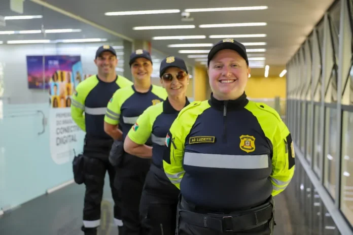 Trânsito de Criciúma adota padrão nacional de uniformes Agentes de trânsito de Criciúma em fila vestindo os novos uniformes nas cores amarelo neon e preto, com detalhes refletivos e o brasão do município para maior segurança viária.