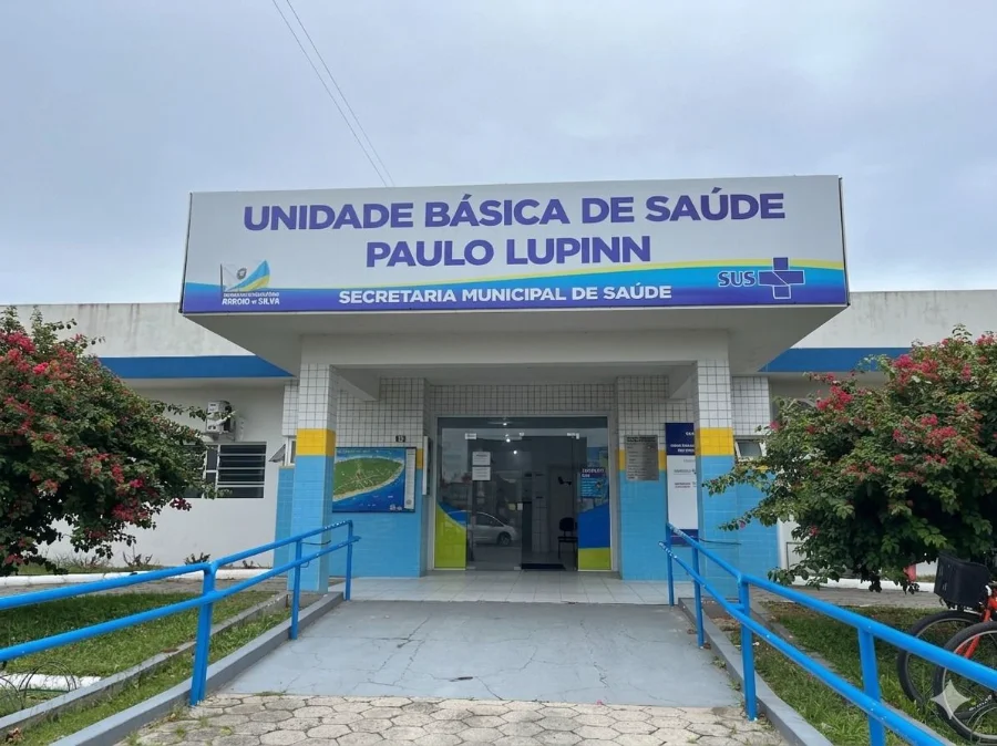 UBS Paulo Lupinn amplia atendimento em Arroio do Silva Fachada da Unidade Básica de Saúde (UBS) Paulo Lupinn, o Posto Central de Balneário Arroio do Silva, mostrando a entrada com rampa de acessibilidade azul, paisagismo e a placa de identificação. A imagem representa o local que passará a ter horário estendido para a saúde do trabalhador.