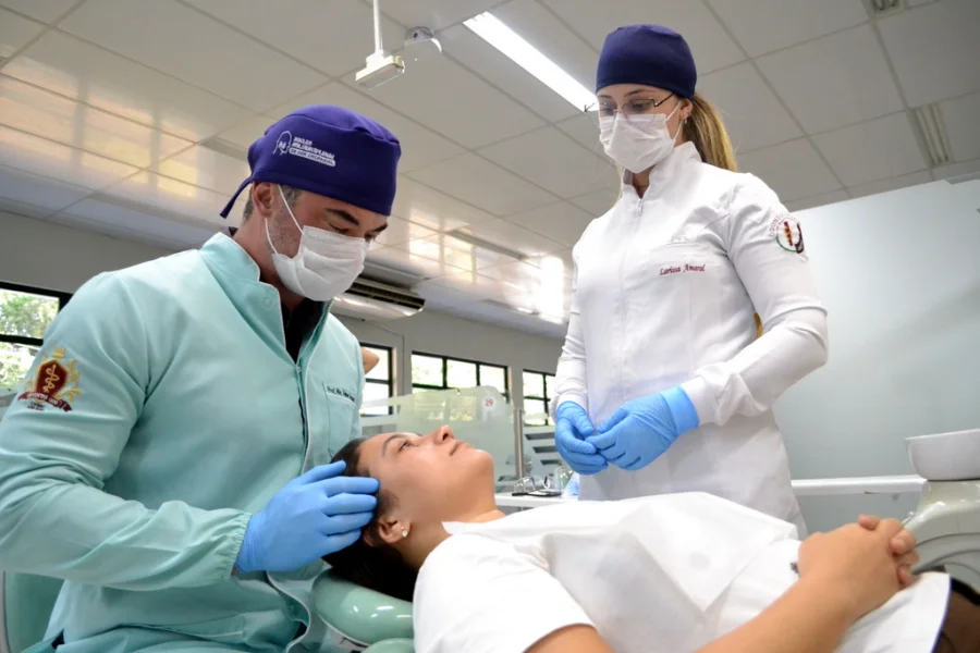 O cirurgião-dentista e professor Felipe Veronez realiza exame clínico em paciente no Núcleo de Dor Orofacial (Nudof) da Unesc para diagnóstico de bruxismo e tensões musculares. Ao lado, a acadêmica Larissa Amaral acompanha o procedimento em ambiente odontológico.