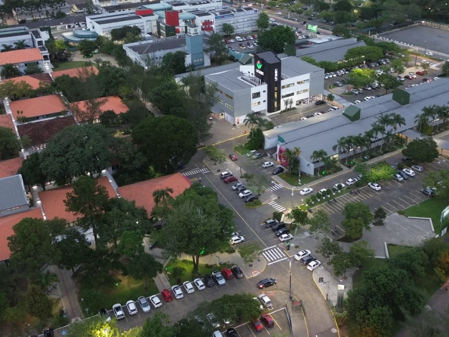 Vista aérea do campus da Unesc em Criciúma, Santa Catarina, mostrando os blocos universitários, estacionamento com veículos e áreas verdes ao entardecer. A imagem ilustra a unidade que terá horários de funcionamento alterados durante o feriado de Tiradentes.