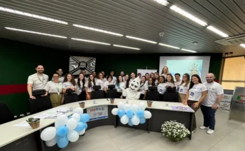 Unesc e Criciúma lançam projeto de imersão no SUS Grupo de acadêmicos de saúde da Unesc e profissionais reunidos no Paço Municipal de Criciúma para o lançamento do projeto VER-SUS/Brasil. A imagem mostra cerca de 30 pessoas com camisetas brancas do projeto, posicionadas atrás de uma bancada com balões azuis e brancos e a presença do mascote Zé Gotinha ao centro.