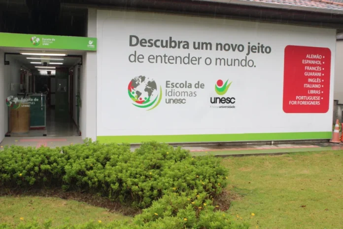 Unesc lança curso de italiano para área da saúde Fachada da Escola de Idiomas da Unesc com painel informativo listando cursos como italiano, inglês e espanhol. A imagem destaca a entrada da unidade onde será realizado o curso de italiano para profissionais da saúde.