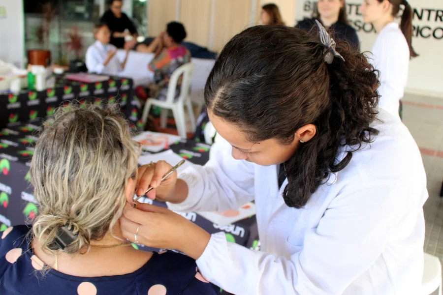 Profissional de saúde com jaleco branco realiza aplicação de auriculoterapia em paciente durante evento de práticas integrativas na Semana da Saúde da Unesc.