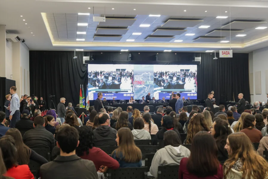 Alesc Itinerante reúne 1,5 mil pessoas em Araranguá Plenário do programa Alesc Itinerante em Araranguá com público assistindo à sessão da Assembleia Legislativa de Santa Catarina no Centro Multiuso Arlete Cristiano Salomé. Ao fundo, grande painel de LED exibe a transmissão do evento e a identidade visual do projeto.