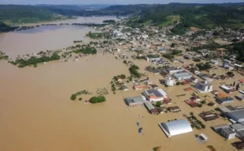 Alesc debate prevenção a chuvas intensas em SC Área urbana alagada em Santa Catarina após chuvas intensas, com ruas, casas e prédios cercados pela água durante enchente