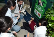 Alunos de Enfermagem da Unesc treinam emergência em campus Estudantes de enfermagem da Unesc realizando atendimento de emergência simulado em vítima de trauma com colar cervical e seringa no chão durante atividade prática no campus.
