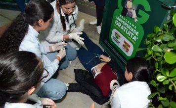 Alunos de Enfermagem da Unesc treinam emergência em campus Estudantes de enfermagem da Unesc realizando atendimento de emergência simulado em vítima de trauma com colar cervical e seringa no chão durante atividade prática no campus.
