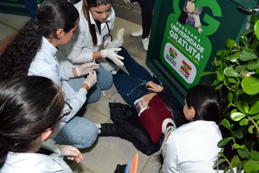 Estudantes de enfermagem da Unesc realizando atendimento de emergência simulado em vítima de trauma com colar cervical e seringa no chão durante atividade prática no campus.