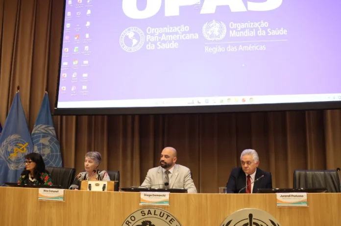 Brasil aprova nova Política de Segurança do Paciente Diogo Demarchi, secretário de Saúde de Santa Catarina, sentado à mesa diretiva durante a assembleia do Conass em Brasília. Ao fundo, um telão exibe as logomarcas da OPAS e OMS. A imagem foca na discussão sobre a Política Nacional de Segurança do Paciente e saúde mental no SUS.