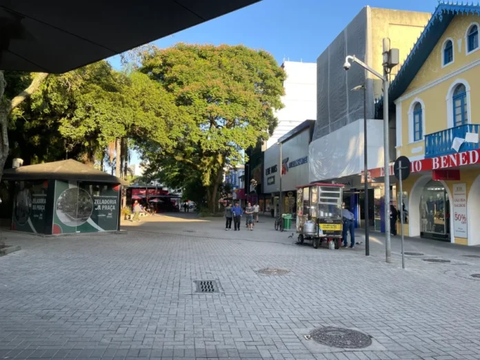 Comércio de Criciúma projeta alta nas vendas do Dia das Mães Vista da Praça Nereu Ramos no centro de Criciúma com pedestres circulando entre lojas e comércios locais em dia ensolarado. Foco no calçadão comercial de Criciúma preparado para as vendas do Dia das Mães.