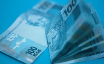 Endividamento das famílias bate recorde histórico em 2026 Cédulas de 100 reais em destaque com iluminação azulada, ilustrando a crise financeira, o endividamento recorde das famílias brasileiras e a pressão sobre a renda mensal em 2026.