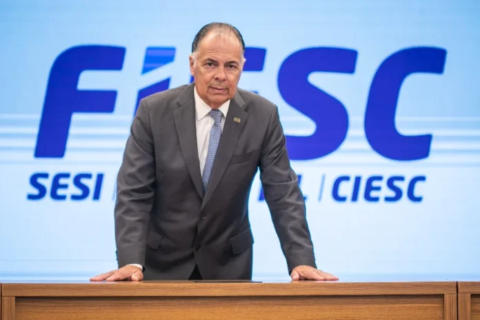 FIESC critica fim de imposto para compras de até US$ 50 Presidente da FIESC, Gilberto Seleme, em frente ao painel da entidade, em manifestação sobre imposto de importação para compras internacionais.