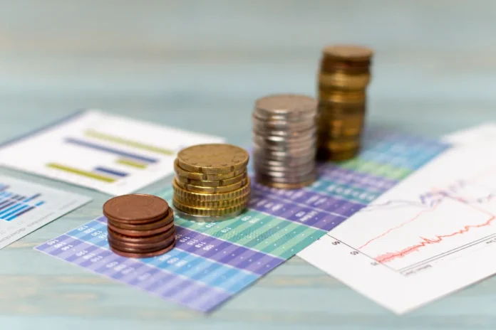 Focus prevê inflação maior e PIB menor Pilhas de moedas sobre gráficos financeiros ilustram projeções do Boletim Focus para inflação, PIB e juros no Brasil.