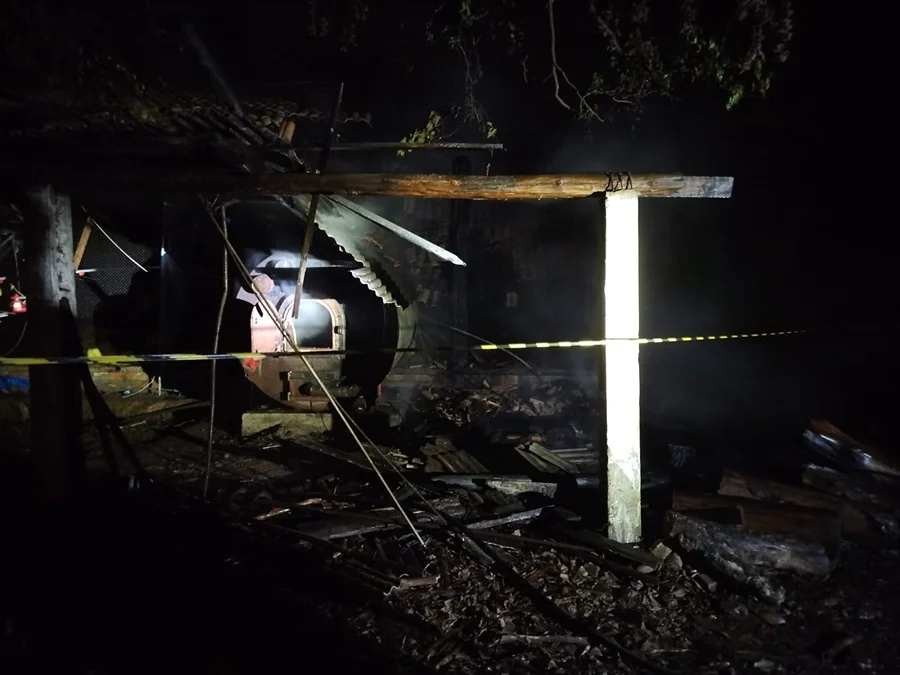 Incêndio destrói aviário em Timbé do Sul na madrugada Estrutura destruída de aviário após incêndio em Timbé do Sul com fita de isolamento e fumaça visível ao fundo