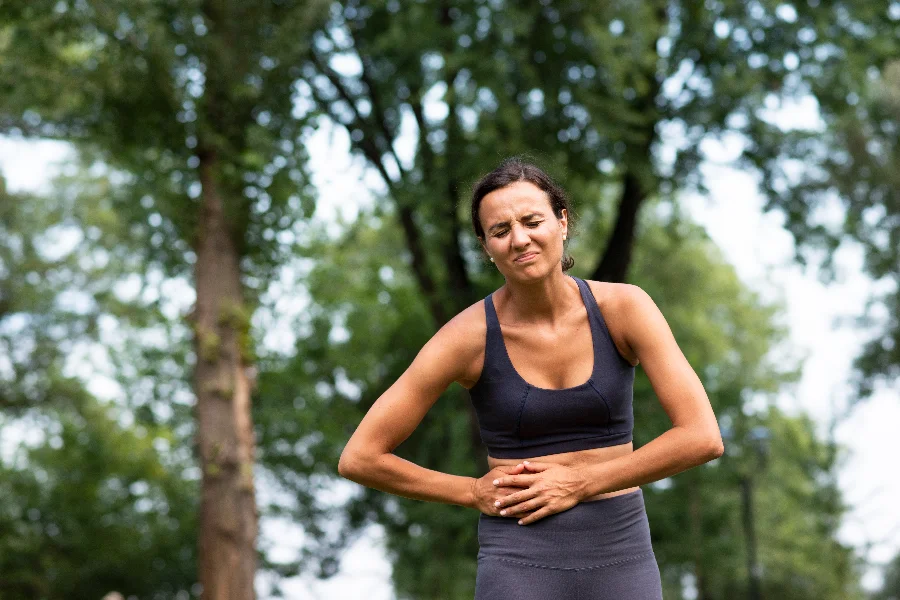 Mulher com dor abdominal em área ao ar livre ilustra sintomas de doenças inflamatórias intestinais durante a campanha Maio Roxo.