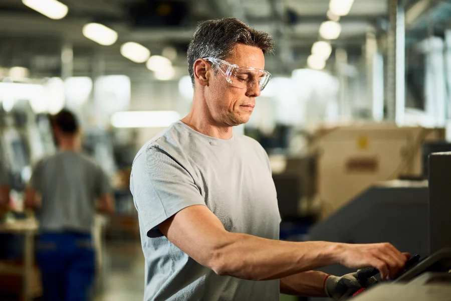 Trabalhador industrial usando óculos de proteção em máquina, em matéria sobre NR-1 e prevenção de riscos no ambiente de trabalho.