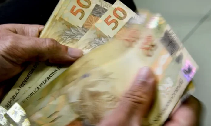 Novo Desenrola Brasil começa nesta terça Mãos seguram cédulas de R$ 50 em imagem sobre renegociação de dívidas no Novo Desenrola Brasil