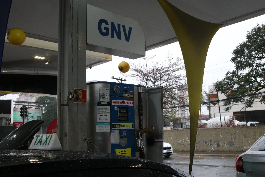 Bomba de abastecimento de GNV em posto de combustível com um táxi em destaque. O reajuste de 19,2% da Petrobras no preço do gás canalizado eleva os custos para motoristas que utilizam gás natural veicular.