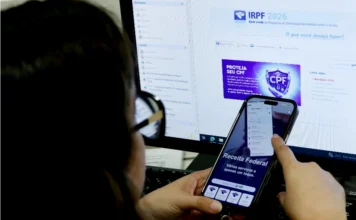 Prazo do IR termina hoje; 5,1 milhões ainda não declararam Pessoa acessa o programa IRPF 2026 da Receita Federal no computador enquanto segura smartphone com aplicativo Meu Imposto de Renda aberto