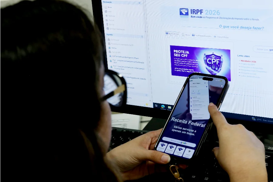 Prazo do IR termina hoje; 5,1 milhões ainda não declararam Pessoa acessa o programa IRPF 2026 da Receita Federal no computador enquanto segura smartphone com aplicativo Meu Imposto de Renda aberto